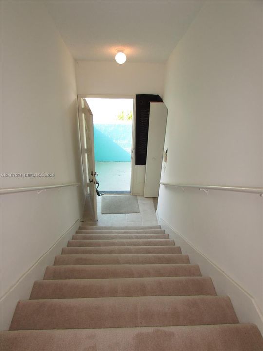 Carpeted staircase featuring white handrails and a flush-mount ceiling light fixture