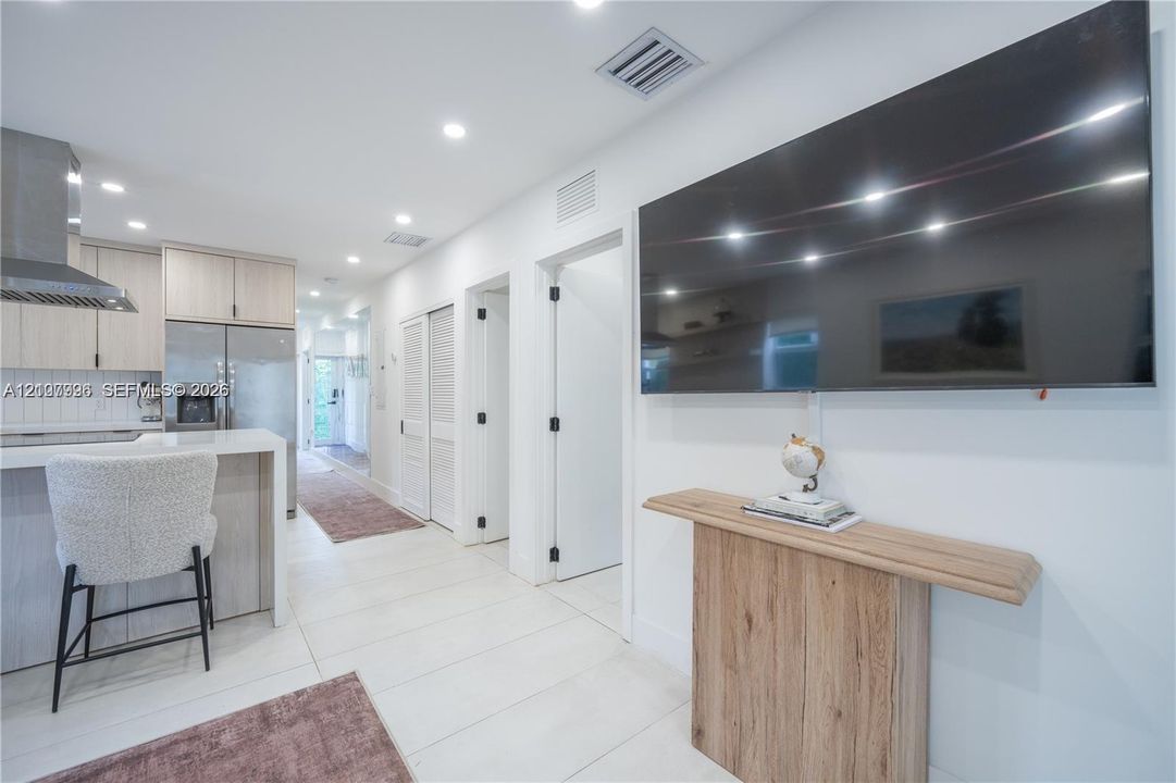 Kitchen featuring light-tone cabinetry, stainless steel appliances, a range hood, and a quartz-topped peninsula with bar seating, complemented by large-format tile flooring and recessed lighting