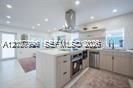 Kitchen featuring a central island with a stone-finish countertop, custom light-toned cabinetry, stainless steel appliances, a chimney-style range hood, and recessed ceiling lighting