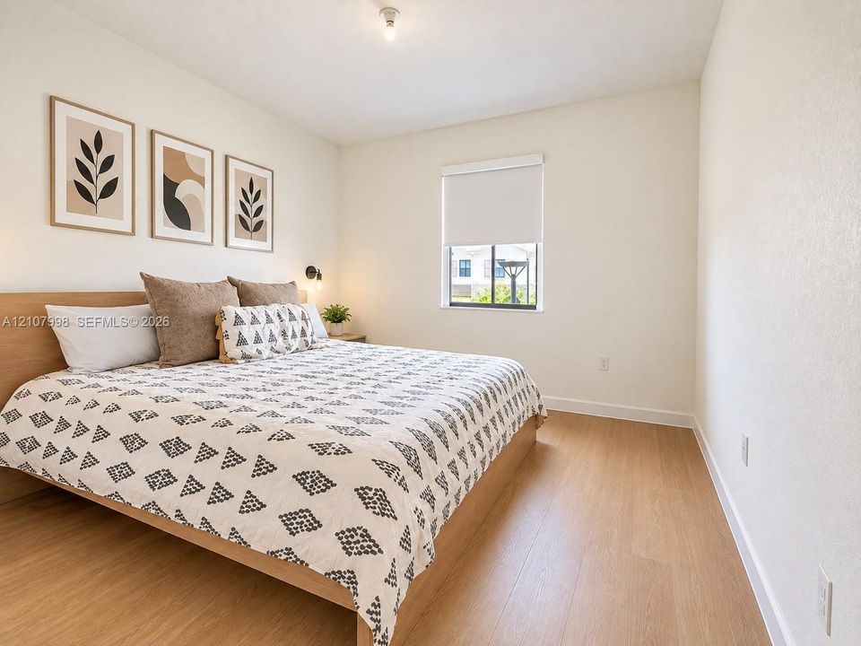 Neutral-toned bedroom featuring wood-finish flooring, a single-pane window with a roller shade, and a built-in wall-mounted light fixture