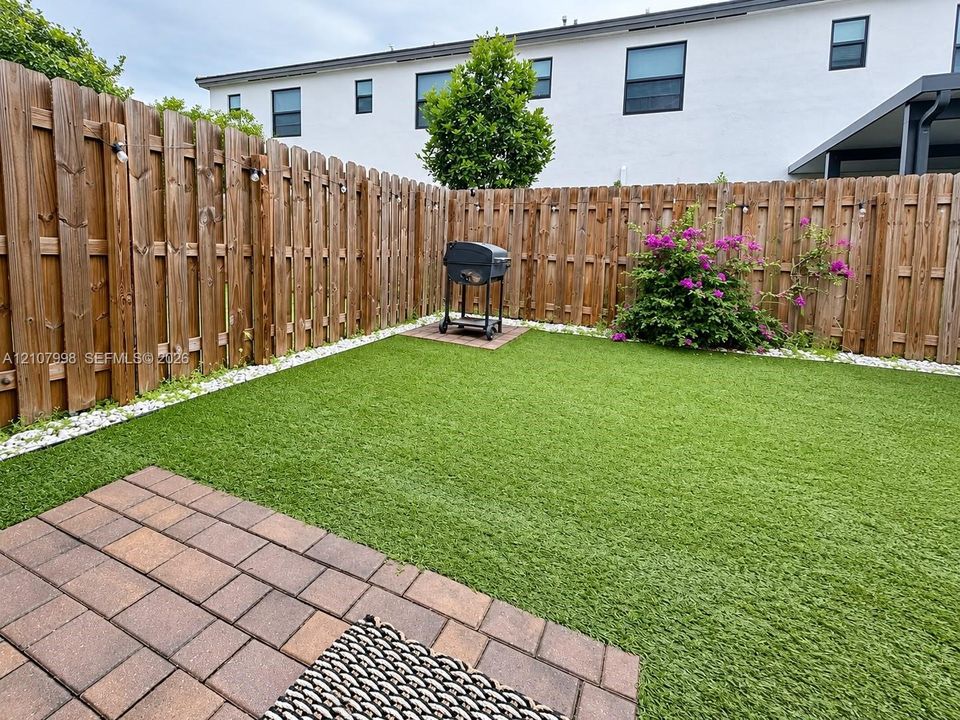 Private backyard featuring synthetic turf, paver patio, stone border, and wood privacy fencing