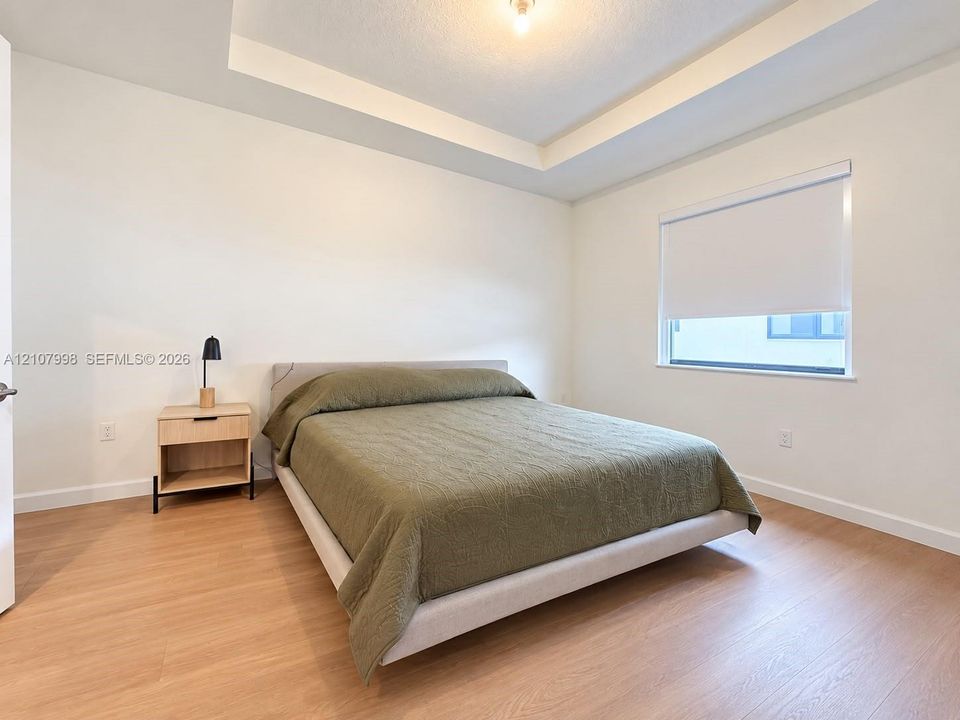 Interior space featuring a recessed tray ceiling, light-tone wood-finish flooring, and a window with a retractable roller shade