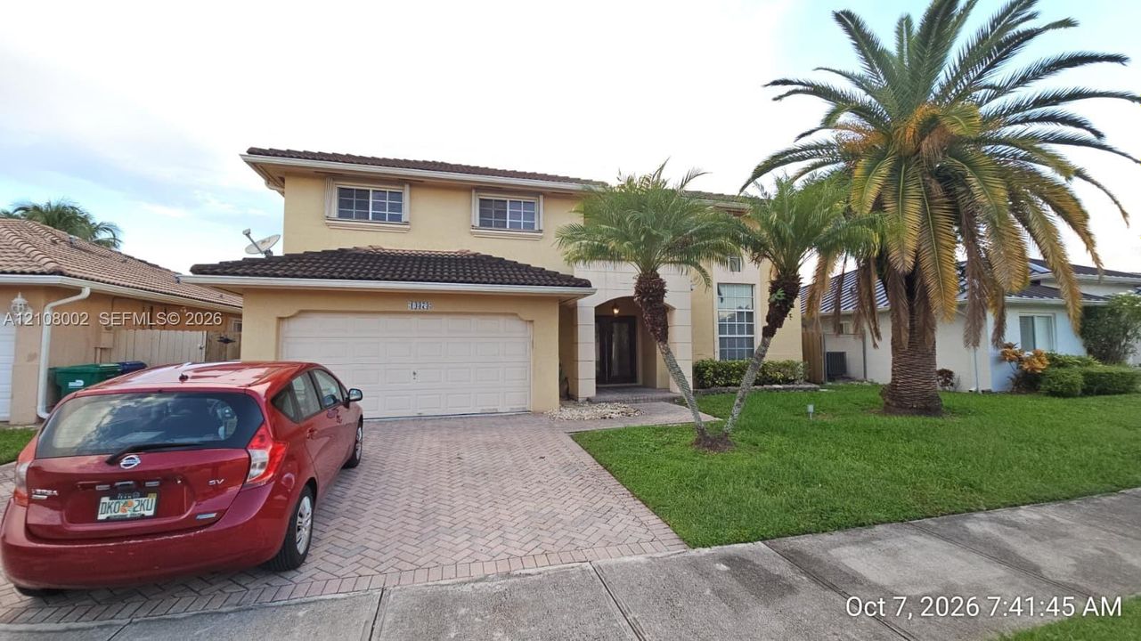 Two-story exterior featuring a stucco facade, tiled roof, arched entryway, brick-paver driveway, and established palm landscaping