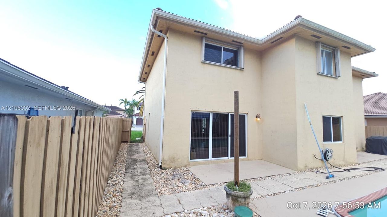 Stucco exterior with sliding glass door access to a concrete patio, stone-surfaced side yard, and wooden privacy fencing