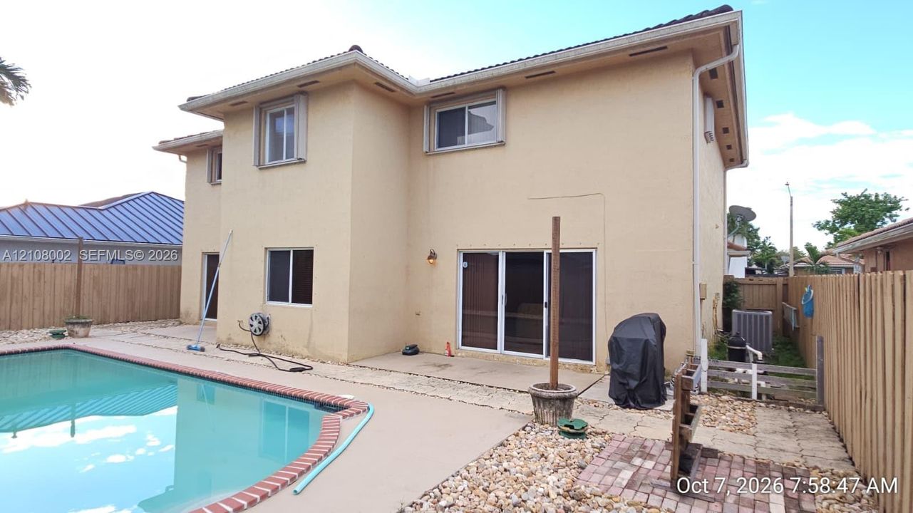 Two-story exterior featuring a stucco facade, a private swimming pool with brick coping, sliding glass doors, and a wood privacy fence