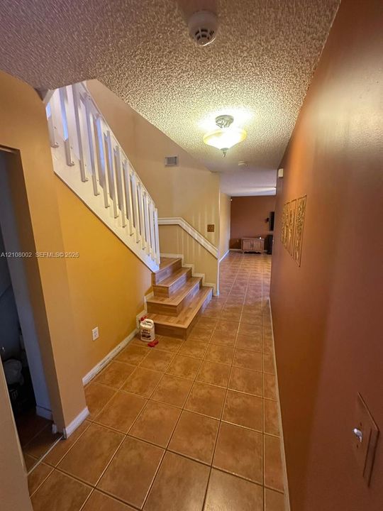 Staircase with white balustrades and wood-finish treads, complemented by large-format ceramic tile flooring and a flush-mount overhead light fixture