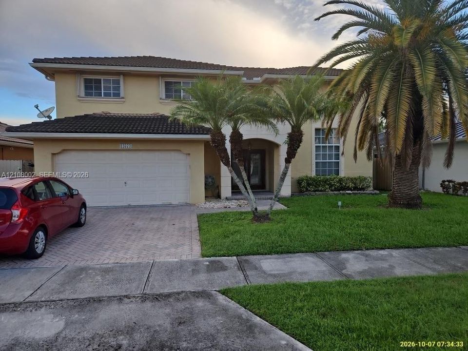 Two-story exterior featuring a tile roof, stucco finish, arched entryway, brick-paver driveway, and mature palm trees
