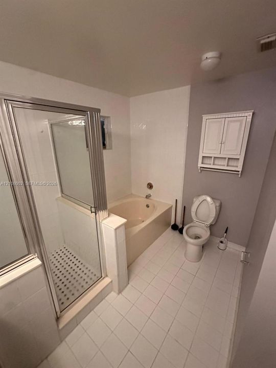 Bathroom featuring a tiled shower enclosure with a glass door, a built-in soaking tub, ceramic tile flooring, and a wall-mounted storage cabinet