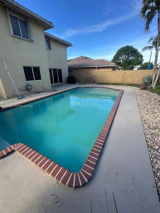 Swimming pool with brick-accented coping, concrete patio, and fenced perimeter