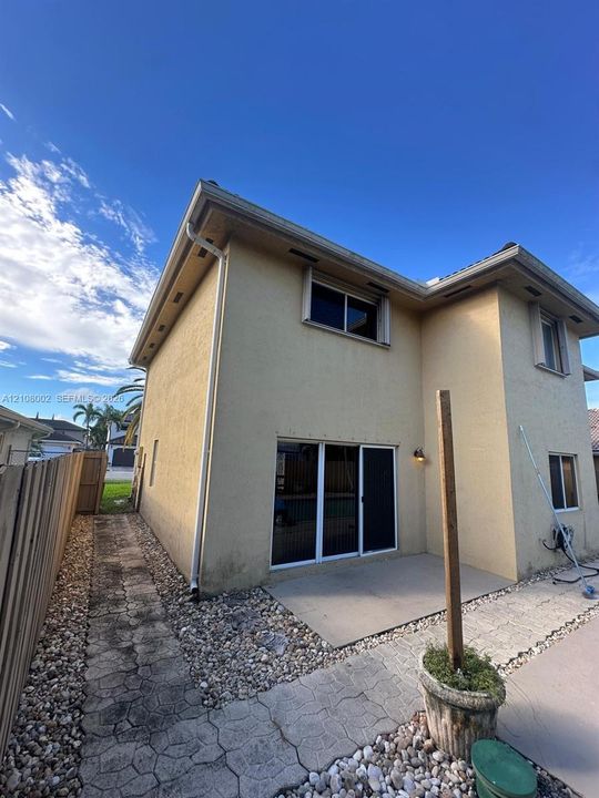 Two-story stucco exterior featuring a rear concrete patio, sliding glass doors, stone-paved walkways, and perimeter wood fencing