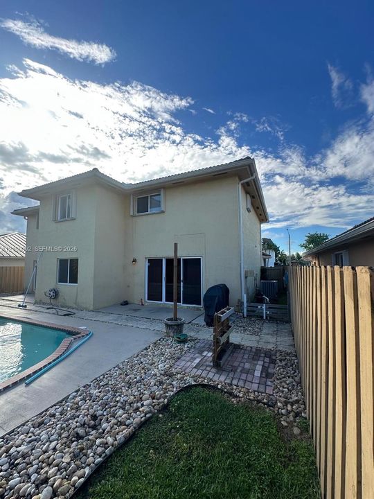 Stucco exterior featuring a sliding glass door, a concrete pool deck, an in-ground swimming pool, and a wood privacy fence
