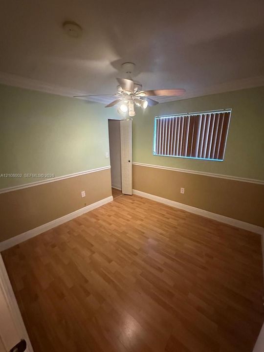 Room featuring wood-finish flooring, two-tone wall paint with chair rail molding, and a central ceiling fan with multi-light fixture