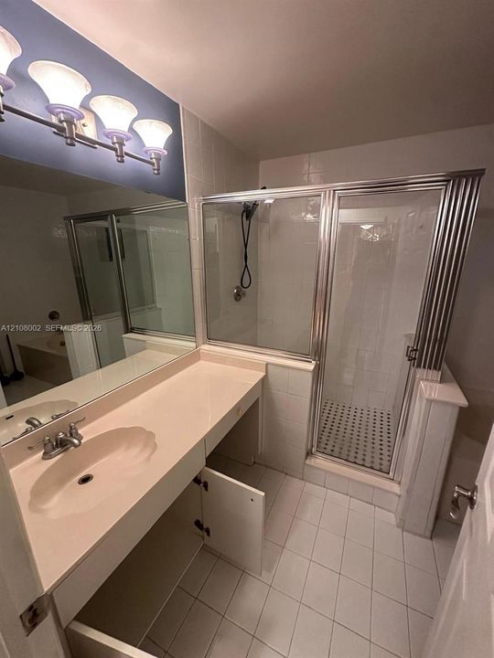 Bathroom featuring a vanity with an integrated basin, a walk-in shower with a metal frame, tile flooring, and a multi-light fixture