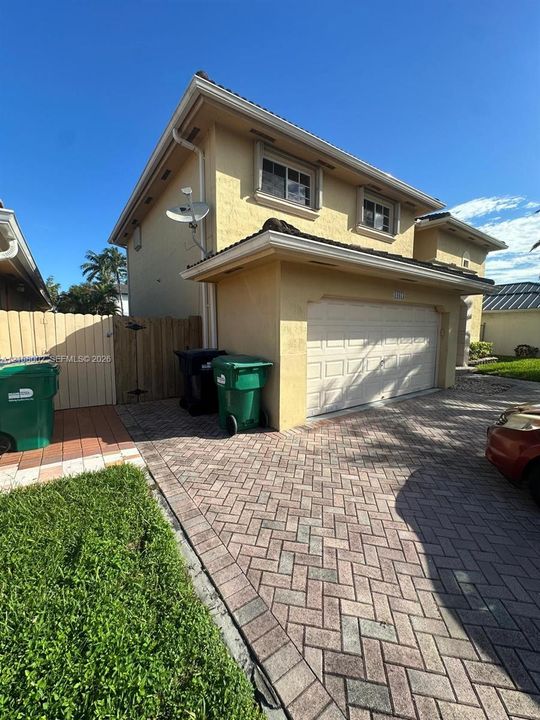 Two-story exterior featuring a stucco facade, herringbone-patterned paver driveway, and a multi-panel garage door