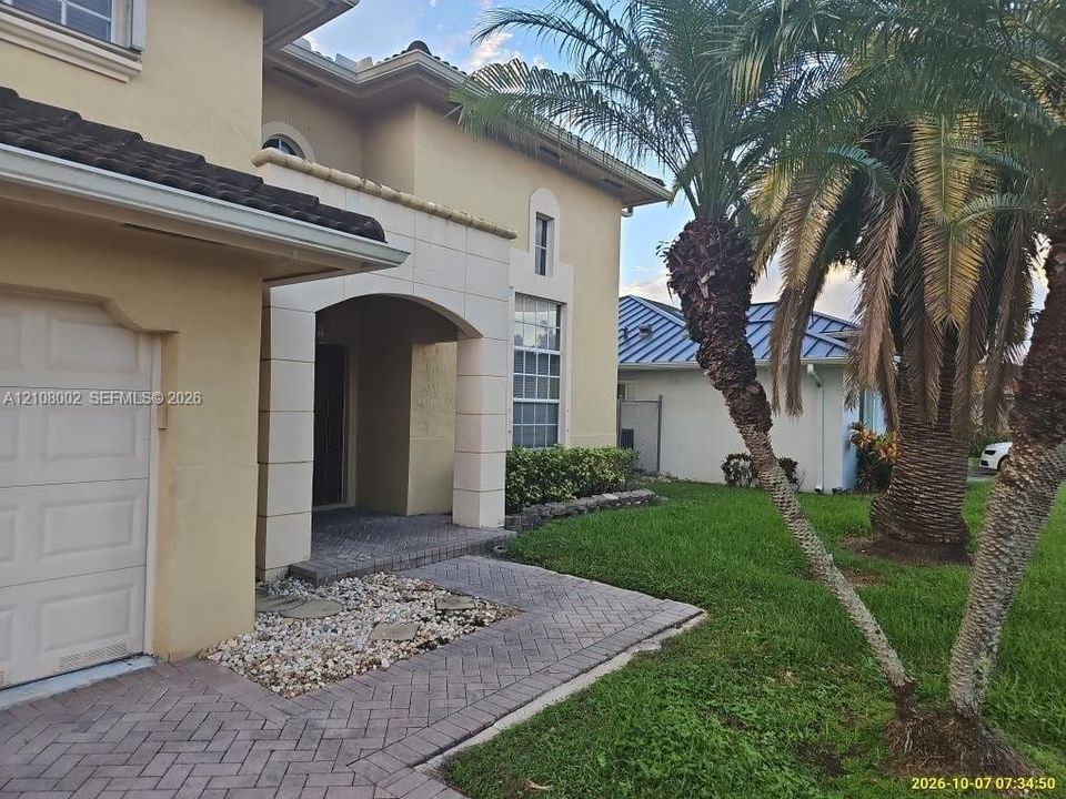 Stucco exterior featuring an arched entryway, stone-tiled walkway, attached garage, and mature palm trees
