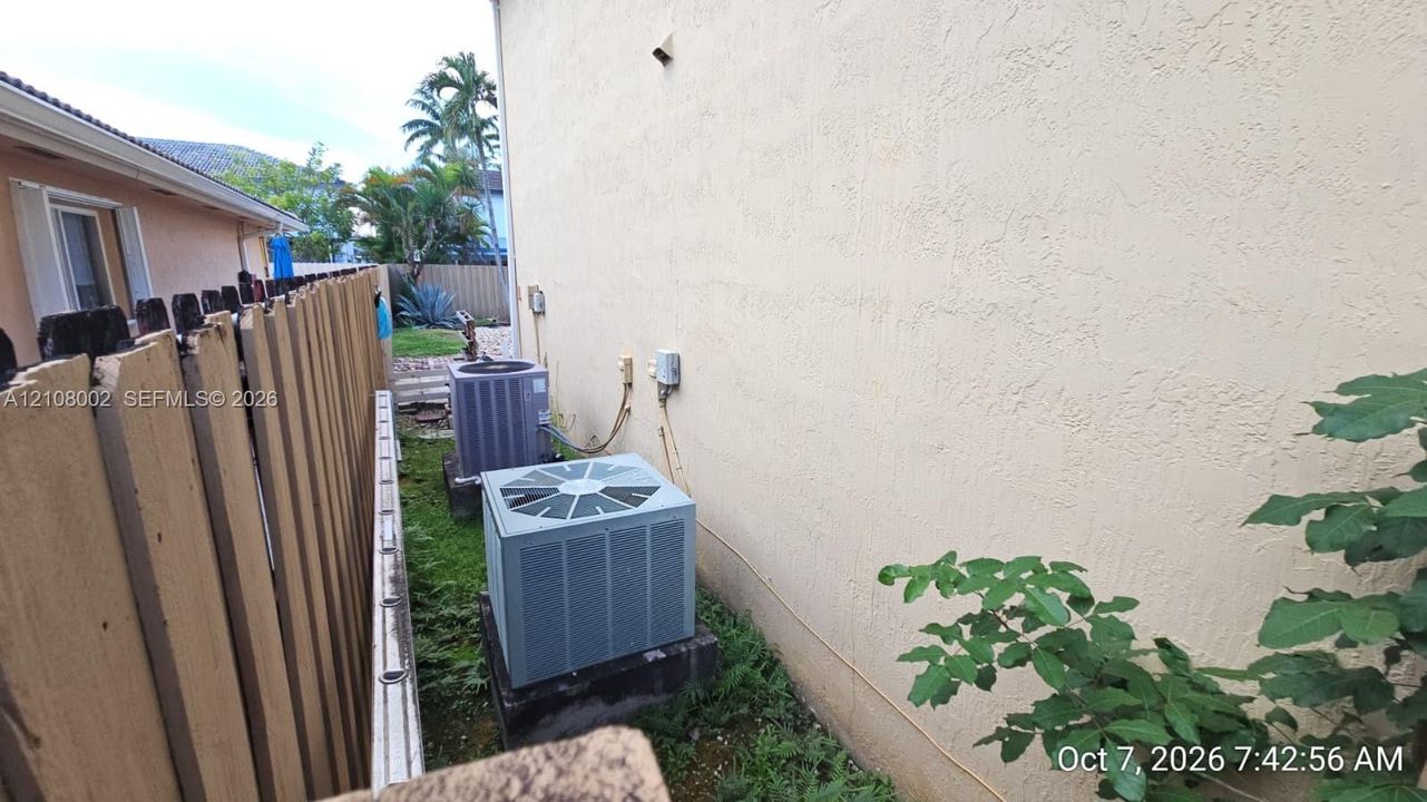 Stucco exterior wall with two ground-mounted HVAC condenser units and perimeter wood privacy fencing