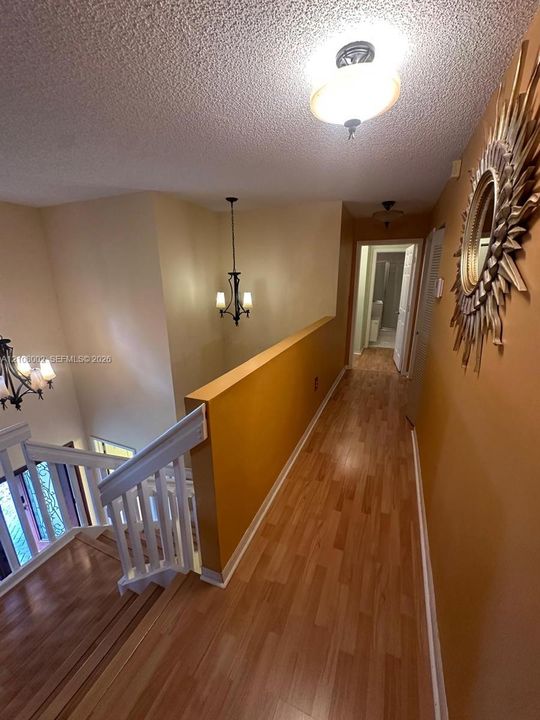 Interior hallway featuring wood-finish flooring, white wooden stair railings, and multiple tiered metal chandeliers with glass shades