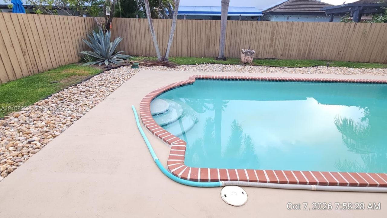 In-ground swimming pool with brick coping and integrated entry steps, surrounded by a concrete deck, decorative rock landscaping, and a wood privacy fence