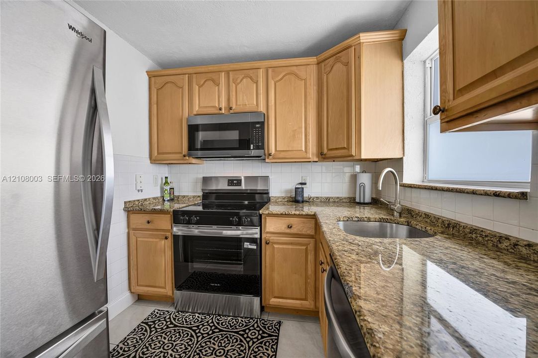 Kitchen featuring light-finish cabinetry, stone-style countertops, stainless steel appliances, a white tile backsplash, and an undermount sink