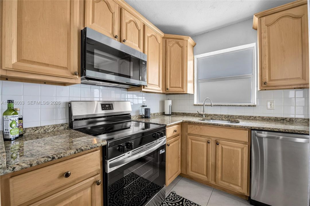 Kitchen featuring natural wood cabinetry, stone-finish countertops, stainless steel appliances, a white tile backsplash, and a metal faucet with an integrated sink