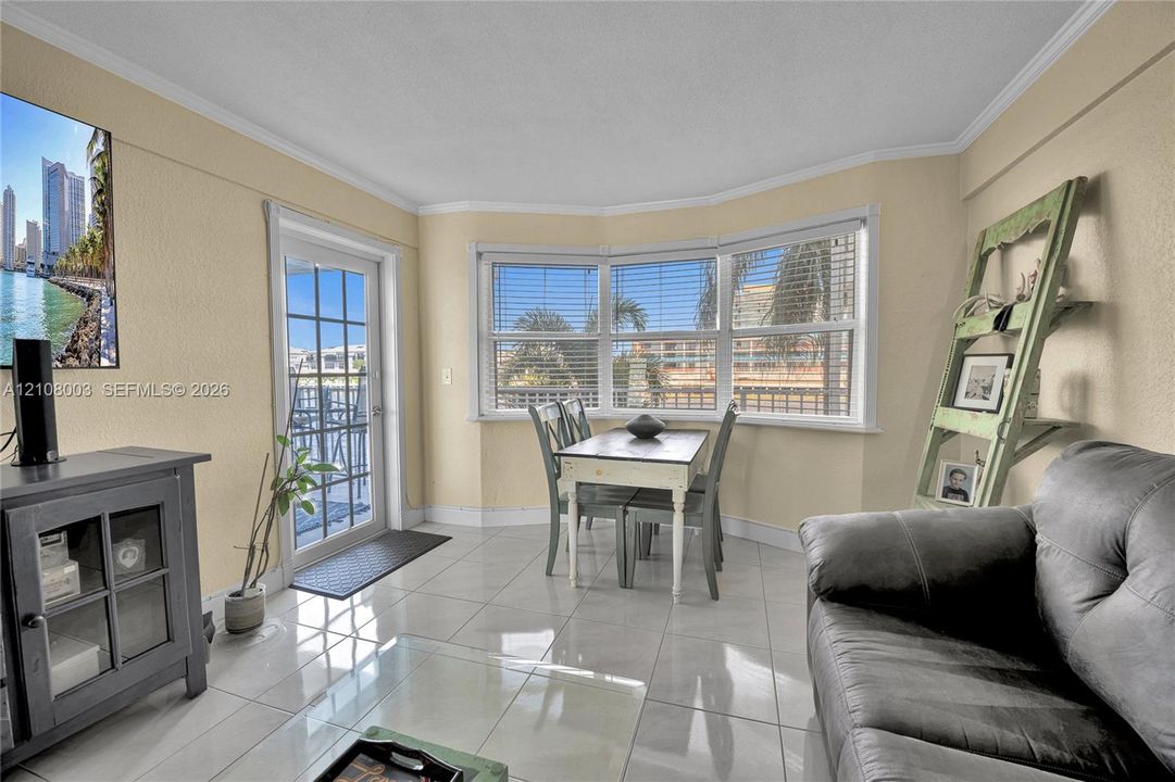 Living area featuring large format tile flooring, crown molding, a multi-panel bay window, and a glass-paned exterior door