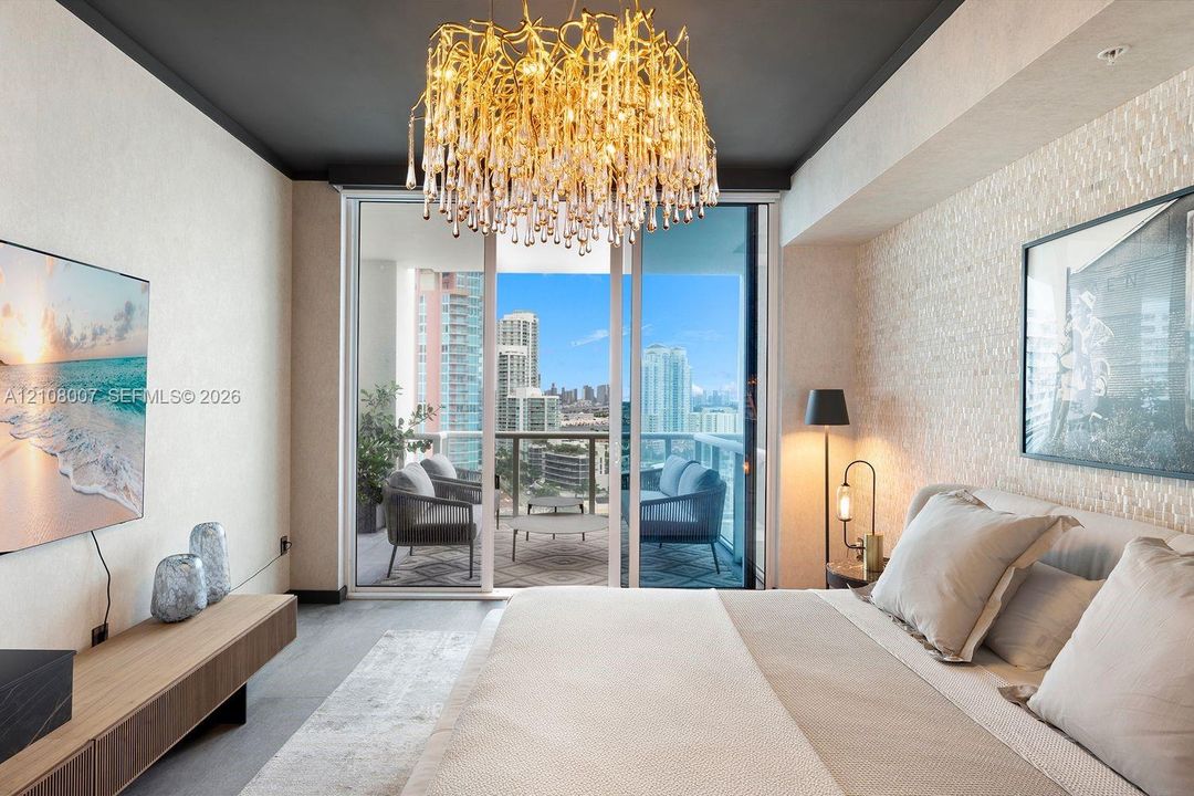 Ornate gold-toned chandelier, floor-to-ceiling glass sliding doors, private balcony, textured stone accent wall, and dark-finished ceiling