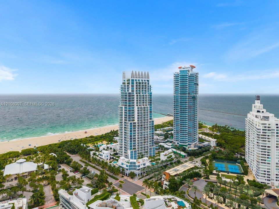 Aerial perspective of coastal high-rise towers featuring floor-to-ceiling glass balconies, beach proximity, and professional-grade tennis courts