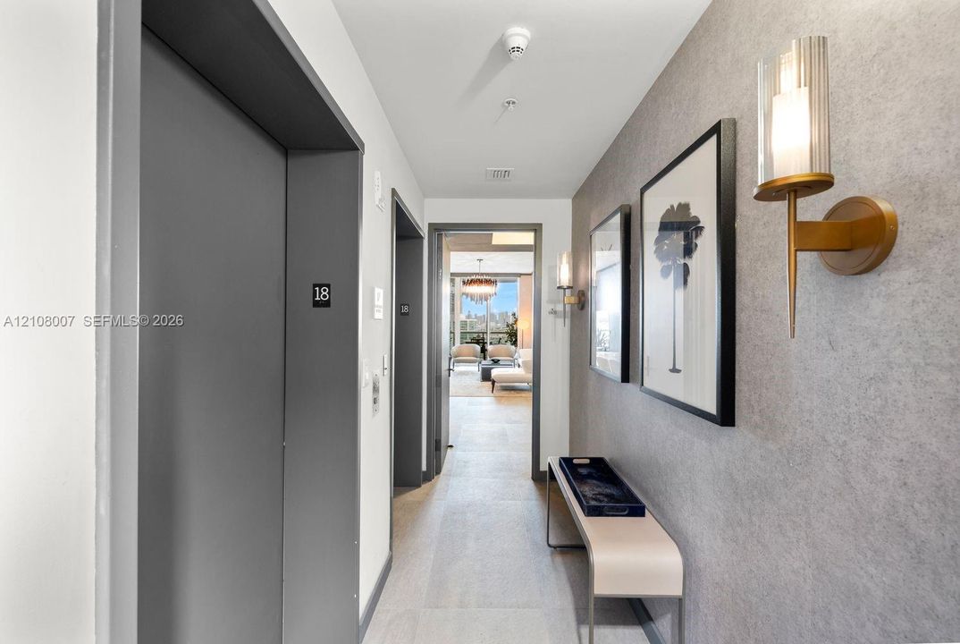 Hallway featuring textured grey wall cladding, gold-toned metallic wall sconces with cylindrical glass shades, and light-toned tile flooring