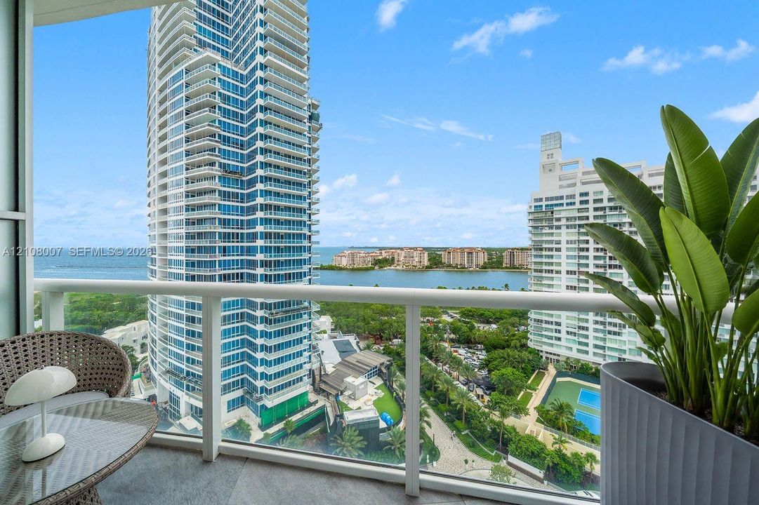 Private covered balcony featuring glass railings and stone flooring, offering expansive water and skyline scenery