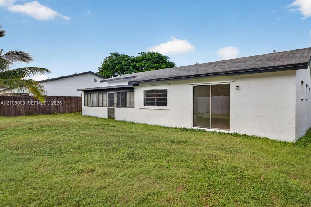 Exterior view of a residence featuring a white stucco facade, a dark-toned shingle roof, a glass sliding door, and a screened-in lanai, set against a fenced perimeter
