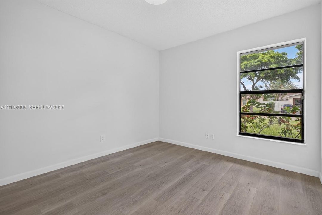 Neutral-toned interior space featuring wood-finish flooring, white walls, and a multi-pane horizontal window