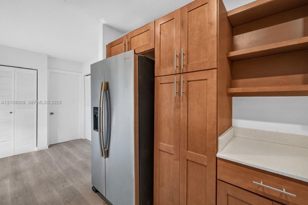 Stained wood cabinetry, stainless steel refrigerator, solid surface countertops, open shelving, and wood-finish flooring
