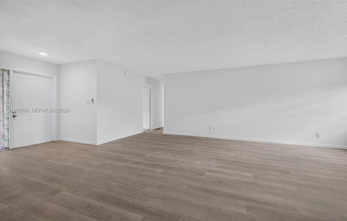 Open-concept interior featuring light wood-finish flooring, neutral wall tones, and an entry door with a six-panel design