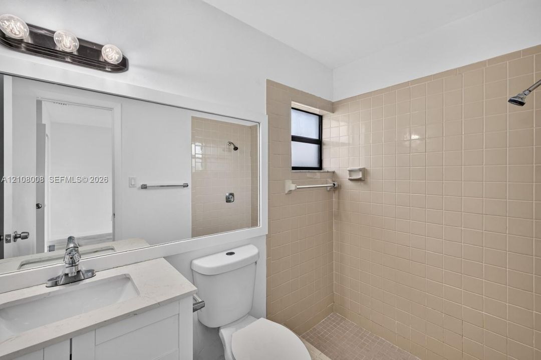 Bathroom featuring a vanity with a solid-surface countertop, rectangular integrated sink, chrome-finish faucet, wall-spanning mirror, and a tiled shower enclosure