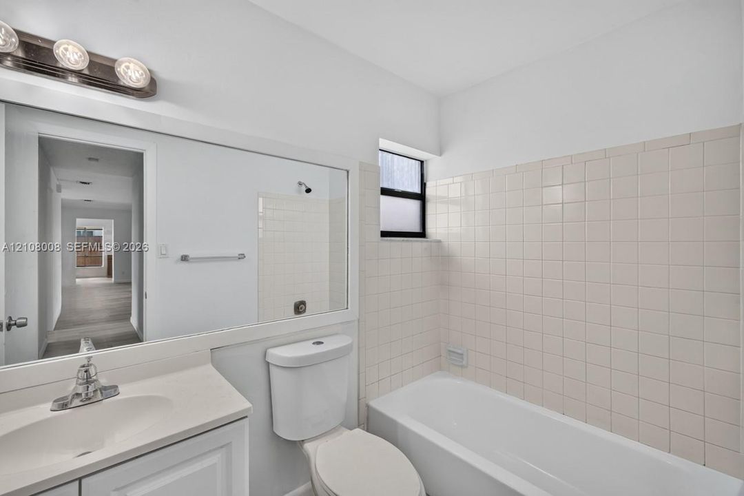 Full-width vanity with integrated sink, expansive wall-mounted mirror, three-light polished chrome fixture, and tiled tub surround