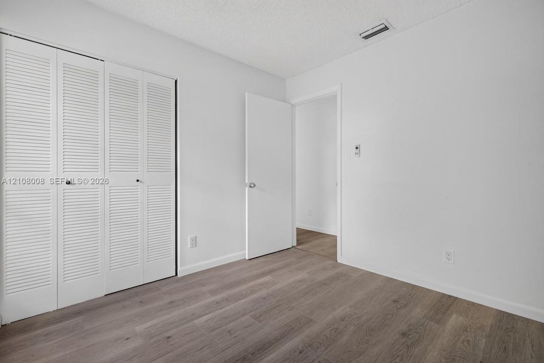 Interior space featuring wood-finish flooring, white walls, and a white louvered closet door