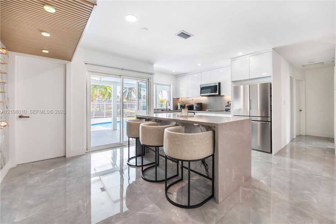 Kitchen featuring high-gloss cabinetry, stone-finish countertops, waterfall-edge island, stainless steel appliances, and large-format tile flooring