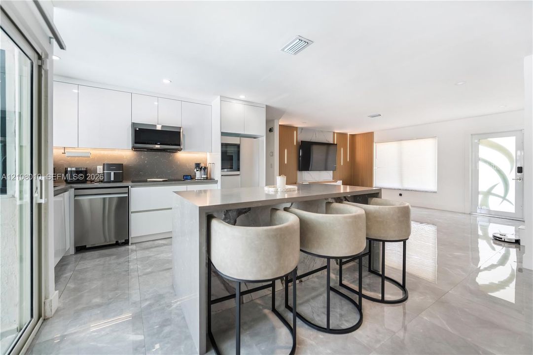 Kitchen featuring high-gloss cabinetry, a waterfall-edge island, polished stone-finish flooring, stainless steel appliances, and integrated under-cabinet lighting