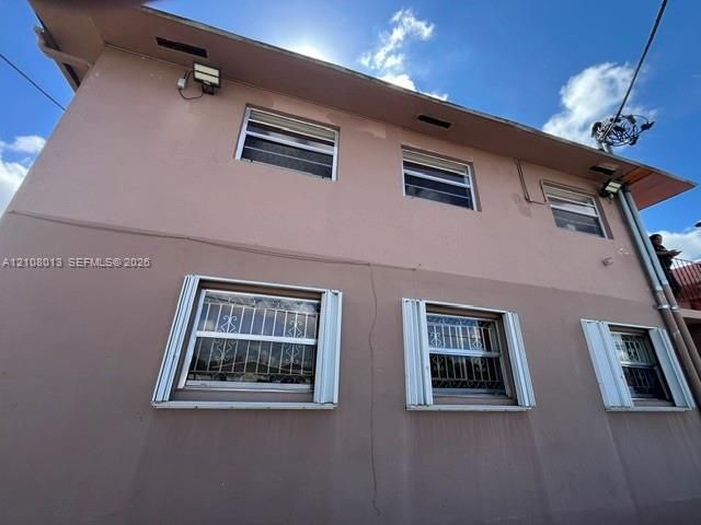 Two-story exterior featuring smooth stucco finish, metal storm shutters on all windows, and integrated security grilles on lower-level windows