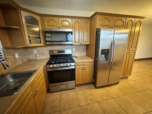 Kitchen featuring natural-finish wood cabinetry, stainless steel appliances, a gas range, a built-in microwave, and tile flooring
