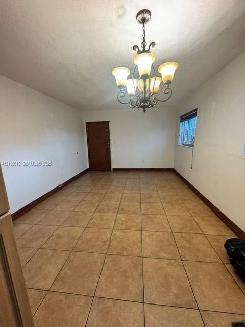 Neutral-toned tile flooring, multi-arm metal chandelier with frosted glass shades, and solid-core wood-finish door