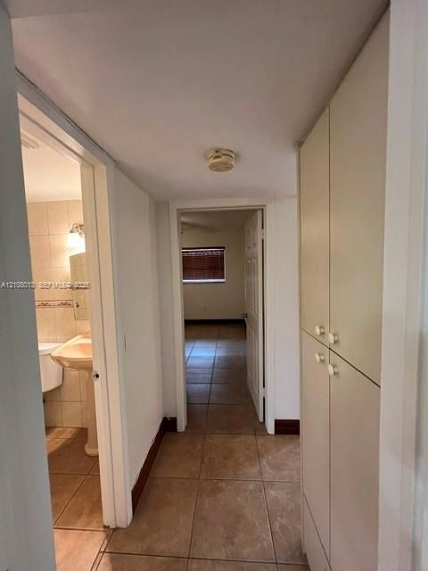 Hallway featuring tile flooring, floor-to-ceiling built-in cabinetry, and a pedestal sink with tile-surround wall finishing