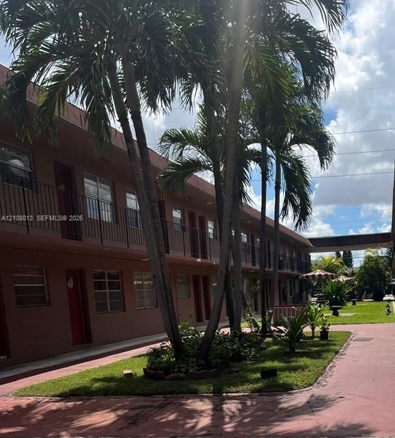 Exterior building facade featuring a two-story design with wrought-iron railings, mature palm trees, landscaped greenery, and paved walkways