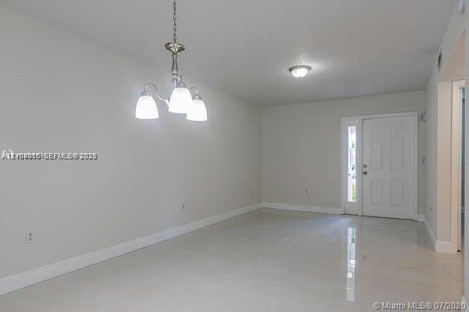 Neutral-toned interior space featuring polished tile flooring, a multi-light brushed nickel chandelier, and a panel-style entry door with an integrated glass sidelight