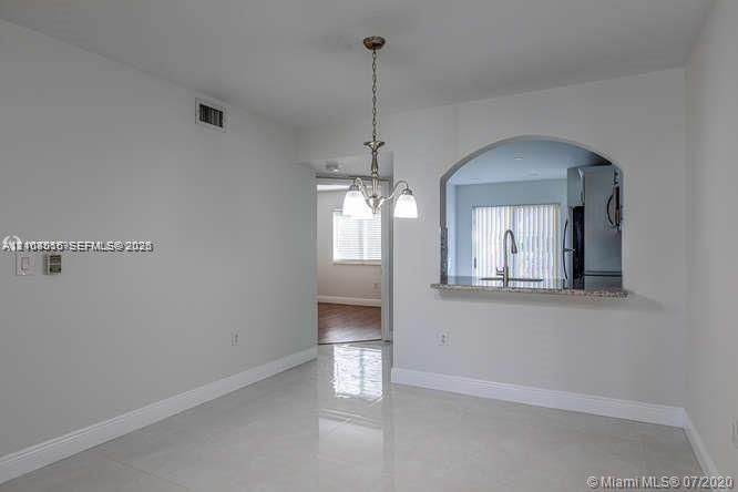 Interior space featuring polished tile flooring, arched wall pass-through with a stone-finish breakfast bar, and a multi-arm metal chandelier