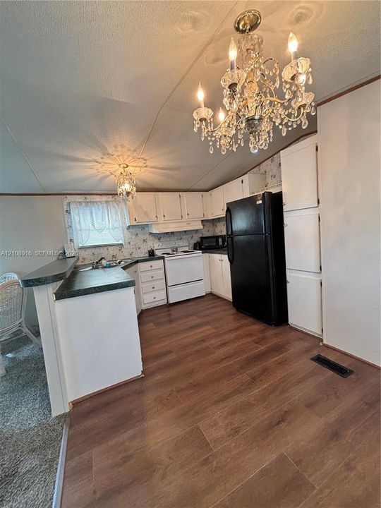 Kitchen featuring wood-finish flooring, white cabinetry, a breakfast bar with stone-finish countertops, and an ornate crystal chandelier