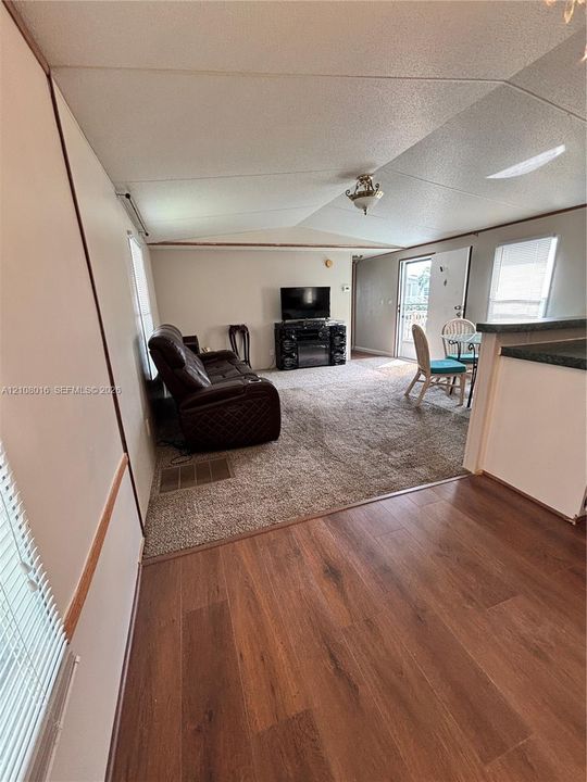 Vaulted ceilings featuring a central flush-mount light fixture, wood-finish flooring, wall-to-wall carpeting, and horizontal window blinds