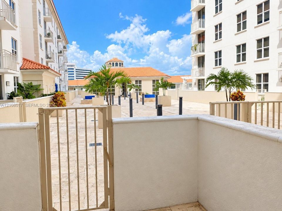 Terrace featuring stone-finish paving, stucco perimeter walls, metal gate entry, and integrated planters with palms