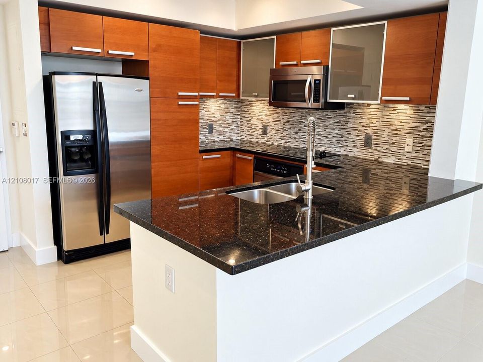 Kitchen featuring flat-panel wood cabinetry, dark stone countertops, stainless steel appliances, multi-tonal mosaic tile backsplash, and a gooseneck faucet