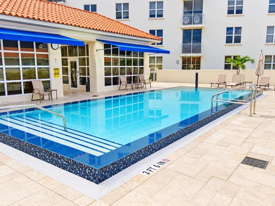 Swimming pool featuring a tiled waterline, built-in entry steps, stainless steel handrails, and surrounding stone paver decking
